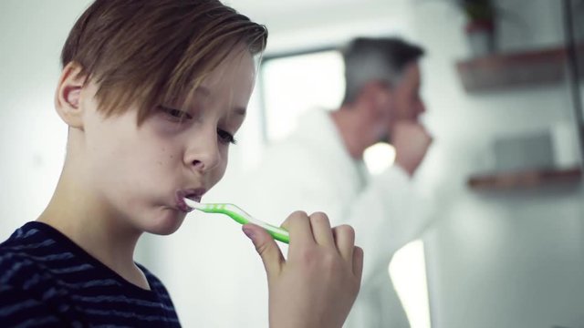 A small son with father brushing teeth in the bathroom in the morning.
