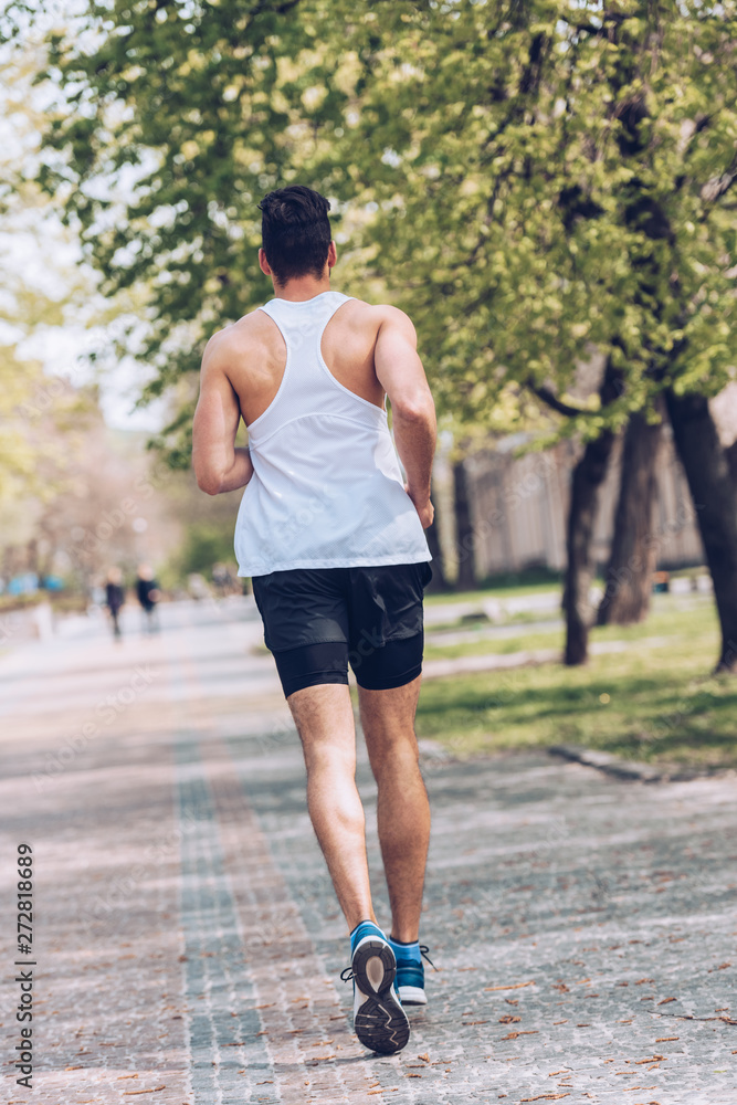 Wall mural back view of young sportsman running along wide alley in park