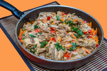 Pieces of rabbit stew with vegetables pepper, onion and herbs in a frying pan on the table. Appetizing delicious food for a festive dinner on a orange background. Horizontal copy space, flatlay