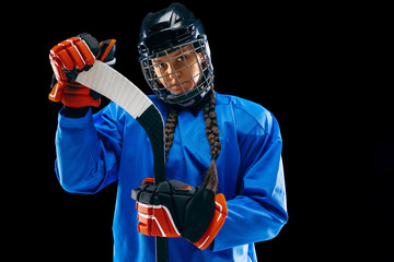 Young female hockey player isolated on black background. Sportswoman wearing equipment and helmet...