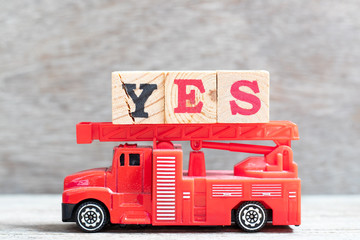 Red fire truck hold letter block in word yes on wood background