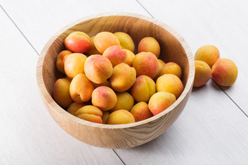 ripe organic apricots fruits in ash tree wooden bowl on a white wooden background