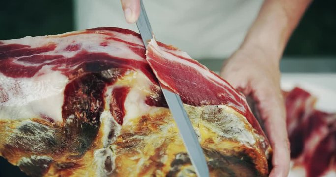 Man slicing jamon leg, a type of dry-cured ham from Spain. Close-up shot on Red