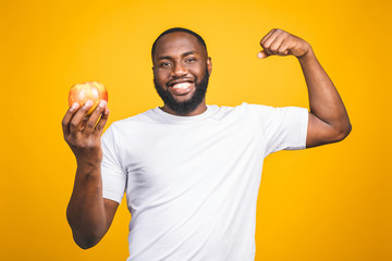 Healthy african american man holding an apple isolated against yellow background.