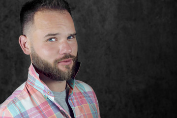Portrait of a young stylish guy with a beard and stylish haircut in a shirt on a gray background with copy space