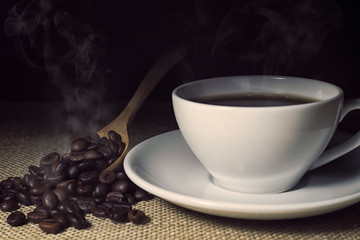 White cup of coffee and steam from a coffee cup,White cup of caffe americano and roasted coffee beans on coffee sack with dark background.
