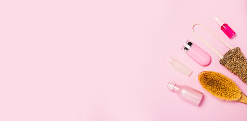 Spa cosmetic background. Bottles, body brush and tropic leaves on pink background. Top view, flat lay.