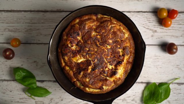 Flat lay of fresh frittata in a cast iron pan turning slowly set against a distressed painted table.