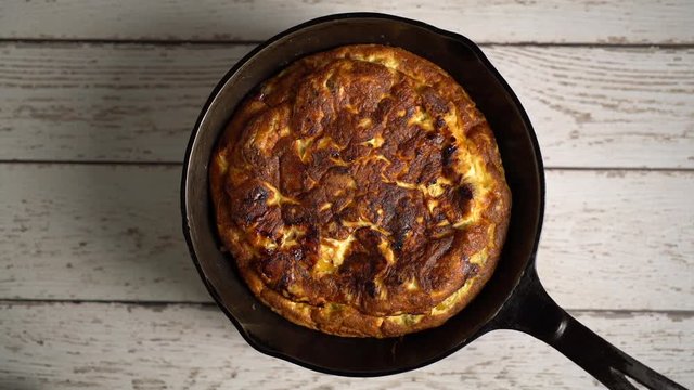 Flat lay of fresh frittata in a cast iron pan turning slowly set against a distressed painted table.