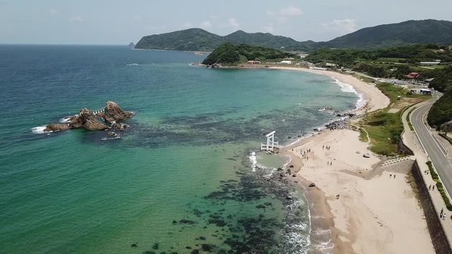 aerial footage, POI, of blue ocean, the twin rocks and the white torii gate on the water at the coast of sakurai futamigaura beach, itoshima fukuoka japan, v02