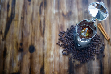 The old  Italian coffee maker,mocha pot placed on wooden table there are roasted coffee beans and cinamon around with warm light in the morning tabletop view