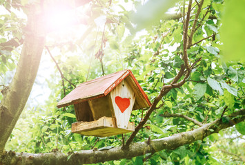 Close up of a lovely little wooden birdhouse with a red heart painted on the front, hanging in a garden