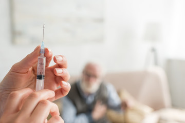 Selective focus of woman hands with syringe on senior man background