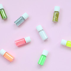 A flat lay pattern with colorful glitter bottles lies on pastel pink background. Many round jars with multi-colored bright sparkles for nail polish. Sparkling sequins. Top view