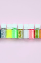 Colorful glitters lies on pastel pink background. Many round jars with multi-colored bright sparkles for nail polish. Sparkling sequins