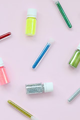 Colorful glitters lies on pastel pink background. Many round jars with multi-colored bright sparkles for nail polish. Sparkling sequins