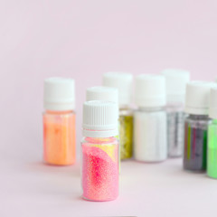 Colorful glitters lies on pastel pink background. Many round jars with multi-colored bright sparkles for nail polish. Sparkling sequins