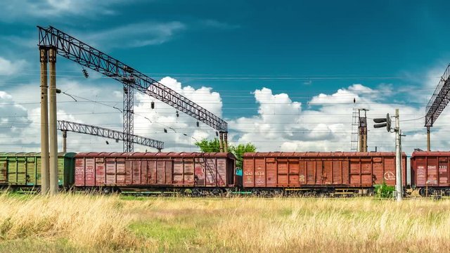 A chain of cargo wagons on a rail road at the background blue sky. Timelapse 4K