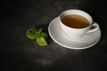 cup of tea on a rough black texture and crescent lime, dark background