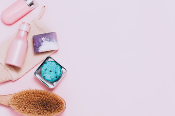 Spa cosmetic background. Bottles, body brush and tropic leaves on pink background. Top view, flat lay.