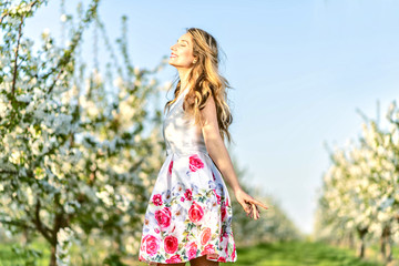 Fototapeta na wymiar Happy Woman in an orchard at springtime. Enjoying sunny warm day. Retro style dress. Blooming blossom cherry trees. Colorful spring moods