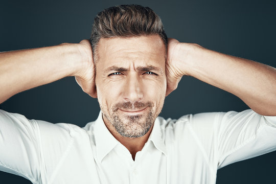 Oh No! Frustrated Young Man Covering Ears With Hands And Making A Face While Standing Against Grey Background