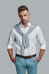 Fototapeta premium Positively charming. Handsome young man looking at camera and smiling while standing against grey background