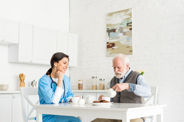 Happy doctor siting on kitchen behind table with senior man