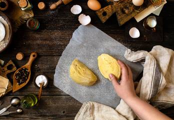 Overhead shot of homemade dough in woman hands on baking paper on rustic table 