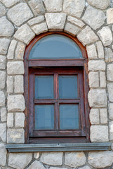 Fototapeta na wymiar Arched wooden window, on a stone wall, with rusticated glass