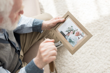 Retired man sitting on couch, and holding photo frame in hand