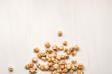 Caramelized popcorn on a white wooden background. Caramel popcorn isolated on white back. Golden caramel popcorn closeup. Snacks and food for a movie.