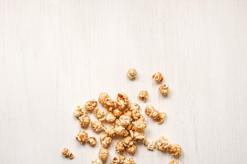 Caramelized popcorn on a white wooden background. Caramel popcorn isolated on white back. Golden caramel popcorn closeup. Snacks and food for a movie.