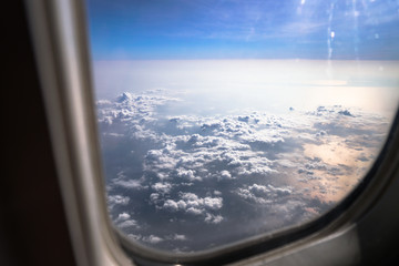 Airplane window overlooking the beautiful clouds and the earth. Sunset in flight on vacation. Tourist theme. Stock photo