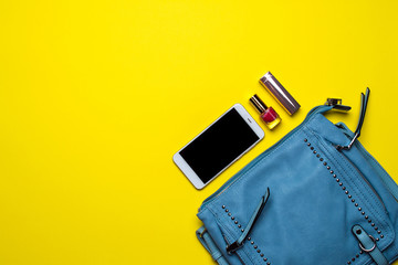 Top view on blue women handbag, smartphone and lipstick with yellow background. Overhead view of ladies bag.