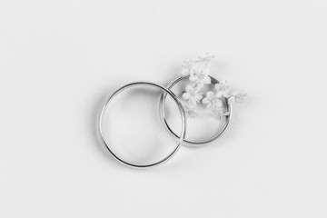 a pair of gold wedding rings and small white flowers in a ring on a white background, top view flat lay, black and white photo