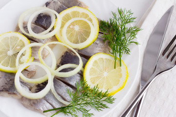 delicious tender herring fillet with lemon,greens and onions on a white plate on a white background