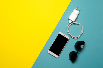 Smartphone plug in with charger usb adapter on yellow and blue background, flat lay, top view