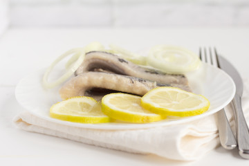 delicious tender herring fillet with lemon and onion on white plate on white background