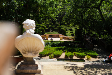 Classic sculpture in the green park. Summertime in spain. The labyrinth from green plants, flowers and trees. Greek sculpture. Arts and beauty. Arks made from greenery. Bokeh, foreground, background