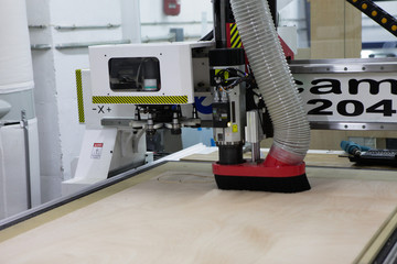 Cutting machine doing matreshka's shapes on plywood. Automated was making shapes on a plane surface. Technology. Wood processing in the manufactory. Red and aluminium details. CNC workshop