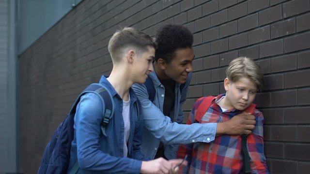 Cruel teen boys pushing junior student, mocking eyeglasses, school bullying
