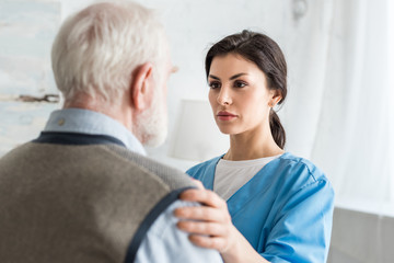 Fototapeta premium Selective focus of serious nurse putting hands on grey haired man
