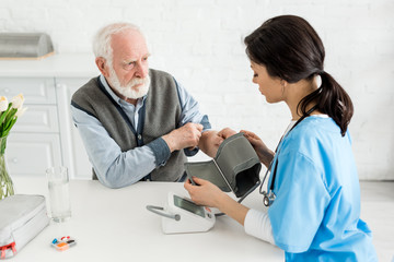 Nurse measuring blood pressure of bearded grey haired man