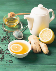 Tea lemon ginger with honey in a white cup and a teapot on a wooden rustic background. Healthy...