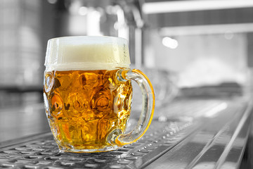 Freshly poured draft lager beer in a dimpled glass mug on stainless steel counter in a modern pub....