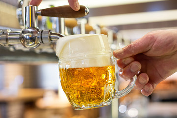 A man pouring draft lager beer into a dimpled glass mug  in a modern pub. Overflowing glass. - obrazy, fototapety, plakaty