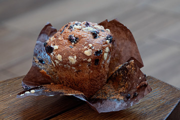 Blueberry muffin unwrapped on brown wax paper on a brown wood table.