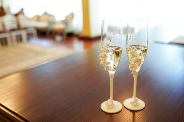 Romantic view of wedding glasses with champagne on dark table with copy space. Two crystal glasses decorated with white flowers. Close-up