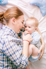 Portrait of beautiful mom in shirt and blue jeans playing with her  baby boy in bedroom